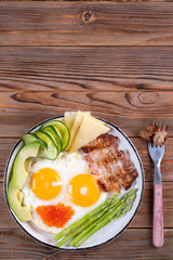Top vertical view of ketogenic diet breakfast on the white plate with a fork on wooden background with copy space