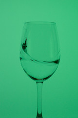 Wine glass on a long stem. A little drink is poured into it, a splash is visible. In back green.