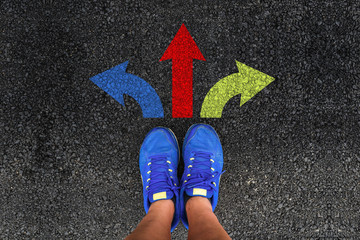 man legs in sneakers standing on road with three direction arrow choices, left, right or move...