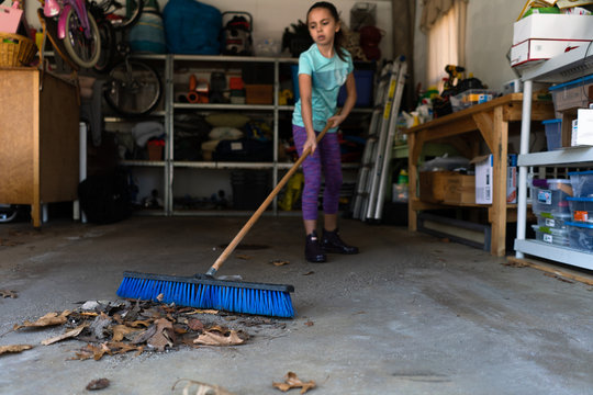 Girl sweeps garage floor with push broom