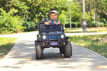 A cute, little boy drives an electric black car in a summer park.	