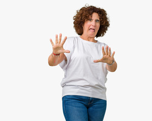 Beautiful middle ager senior woman wearing white t-shirt over isolated background afraid and terrified with fear expression stop gesture with hands, shouting in shock. Panic concept.