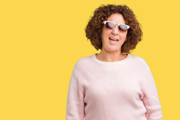 Beautiful middle ager senior woman wearing pink sweater and sunglasses over isolated background...