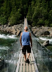 Senior man walking over a suspension bridge in summer