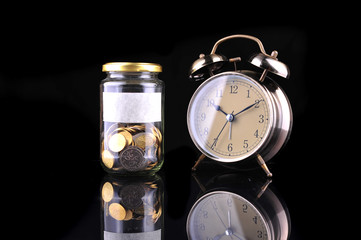 Alarm clock and bottle of coins isolated on black background