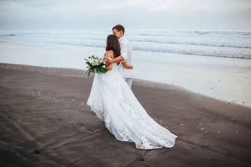 Fototapeta na wymiar Elegant gorgeous bride and groom walking on ocean beach during sunset time.