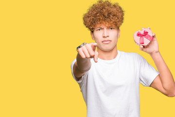 Young handsome man holding heart box as gift of valentine's day pointing with finger to the camera and to you, hand sign, positive and confident gesture from the front