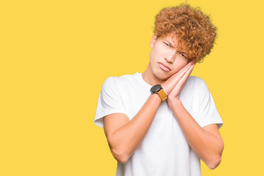 Young handsome man with afro hair wearing casual white t-shirt sleeping tired dreaming and posing with hands together while smiling with closed eyes.