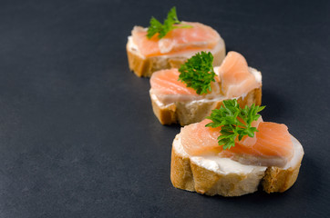 Salmon canape sandwiches with baguette on black grunge background. Canapes with smoked salmon and cream cheese. Salmon sandwich on the black background. 