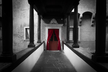 Corridoio con porta rossa al centro con colonne e muratura di un castello del Buon consiglio di Trento
