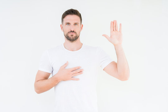 Young handsome man wearing casual white t-shirt over isolated background Swearing with hand on chest and open palm, making a loyalty promise oath