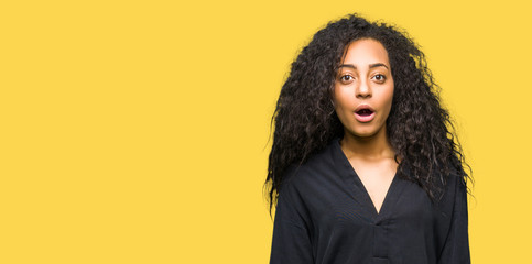 Young beautiful girl with curly hair wearing elegant dress afraid and shocked with surprise...