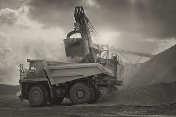 Excavator loads gravel in the dump-body truck, sepia, close-up. Mining industry. Mine and quarry equipment.
