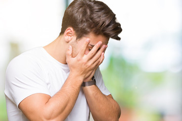 Young handsome man wearing white t-shirt over isolated background with sad expression covering face with hands while crying. Depression concept.