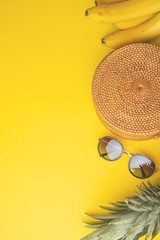 Summer colorful background with wicker fashion bag, women's shoes and tropical pineapple, bananas and sun glasses. Summer fashion, holiday concept. Flat lay. Yellow background. Vertical photo