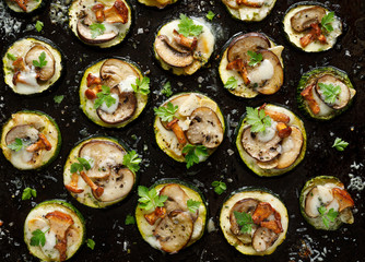Mini pizzas from zucchini slices with the addition of brown mushrooms, mushroom chanterelles, mozzarella cheese and herbs on a black background, top view. Vegetarian food - obrazy, fototapety, plakaty