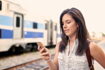 Fototapeta premium Confident millennial student on the go checking her smart phone on a train platform
