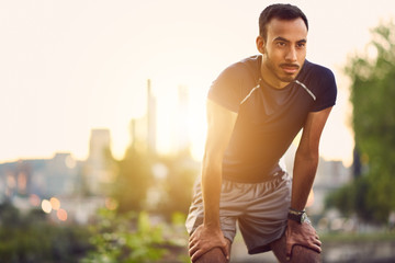 Portrait of active millenial man jogging at dusk with an urban cityscape and sunset in the background