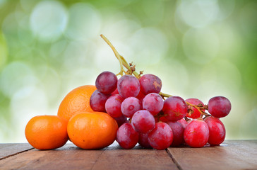 Grapes and Orange on wooden table over green background