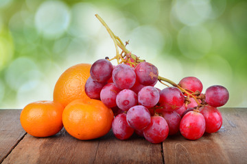 Grapes and Orange on wooden table over green background