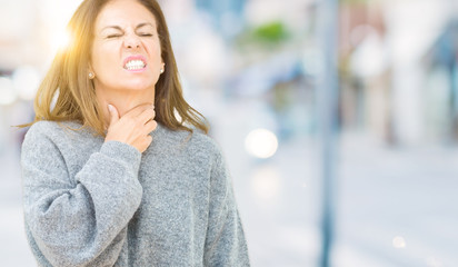 Beautiful middle age woman wearing winter sweater over isolated background Touching painful neck, sore throat for flu, clod and infection