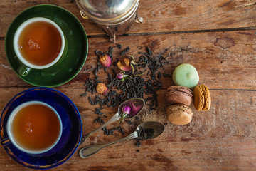 Fototapeta na wymiar Tea time concept. Two vintage cups of black tea, rose buttons, french macaroons on the old wooden background with copy space. Top view