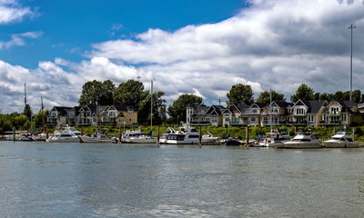 Small Village of new houses  at the riverside of Fraser River, with marina for parking  boats and yachts on the background of cloudy sky