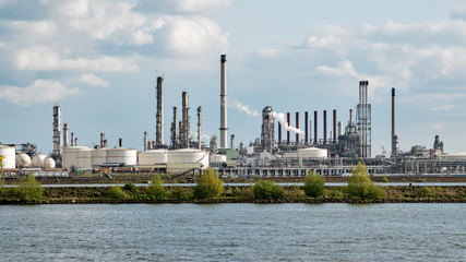 A refinery sprouts chimneys and storage tanks along a river in the Netherlands