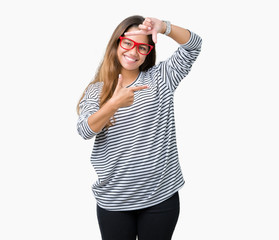 Obraz na płótnie Canvas Young beautiful brunette woman wearing stripes sweater and red glasses over isolated background smiling making frame with hands and fingers with happy face. Creativity and photography concept.