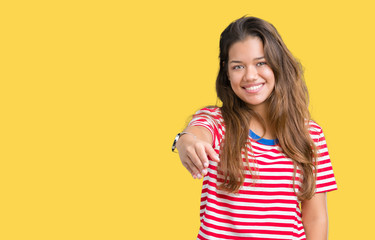 Young beautiful brunette woman wearing stripes t-shirt over isolated background smiling friendly offering handshake as greeting and welcoming. Successful business.
