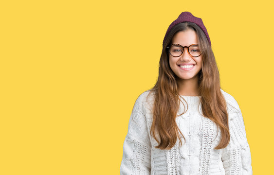 Young beautiful brunette hipster woman wearing glasses and winter hat over isolated background with a happy and cool smile on face. Lucky person.