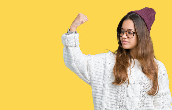 Young beautiful brunette hipster woman wearing glasses and winter hat over isolated background Strong person showing arm muscle, confident and proud of power