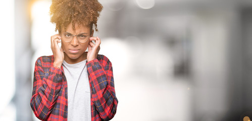 Beautiful young african american woman wearing glasses over isolated background covering ears with fingers with annoyed expression for the noise of loud music. Deaf concept.