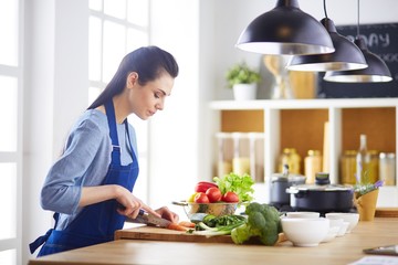 Young woman cutting vegetables in kitchen at home