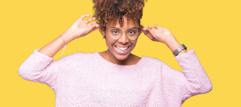 Beautiful young african american woman wearing glasses over isolated background Smiling pulling ears with fingers, funny gesture. Audition problem