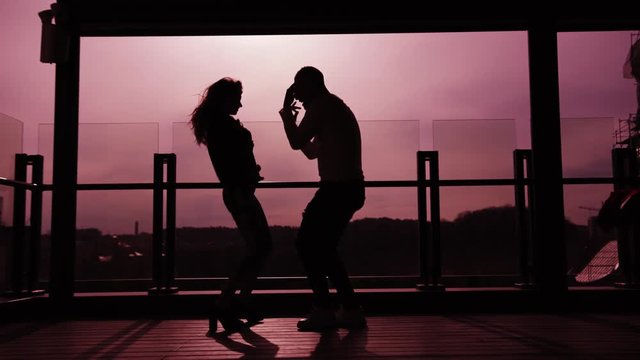 Silhouette of dancing couple on pink sunset background. Two lovers dancing on top of a skyscraper overlooking the city at sunrise/sunset. Romantic atmosphere, date, love. Modern dance