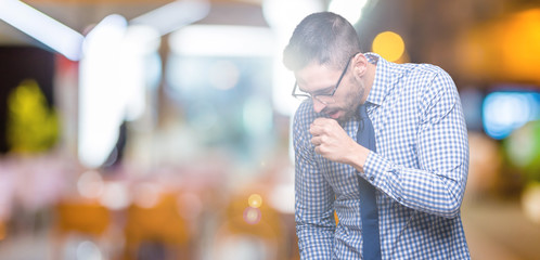 Young business man wearing glasses over isolated background feeling unwell and coughing as symptom for cold or bronchitis. Healthcare concept.