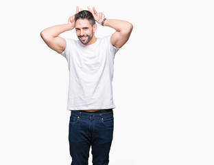 Fototapeta premium Handsome man wearing white t-shirt over white isolated background Posing funny and crazy with fingers on head as bunny ears, smiling cheerful