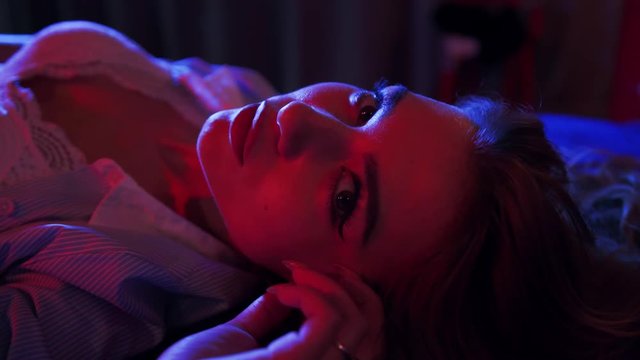 A girl in seductive underwear lies on a bed, poses and looks sexually straight to the camera. Romantic mood, seduction, attraction. Date, confidence. Female portrait, close up view