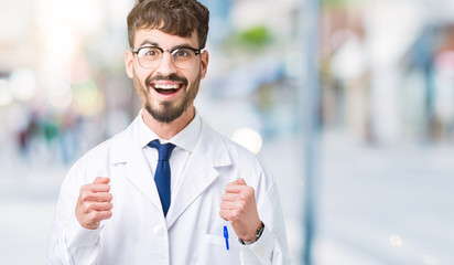 Young professional scientist man wearing white coat over isolated background celebrating surprised and amazed for success with arms raised and open eyes. Winner concept.