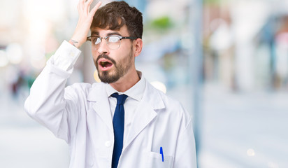 Young professional scientist man wearing white coat over isolated background surprised with hand on head for mistake, remember error. Forgot, bad memory concept.