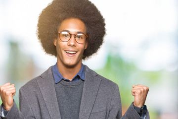 Young african american business man with afro hair wearing glasses celebrating surprised and amazed for success with arms raised and open eyes. Winner concept.