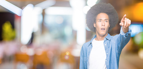 Young african american man with afro hair Pointing with finger surprised ahead, open mouth amazed expression, something in front