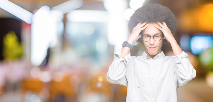 Young african american man with afro hair wearing glasses with hand on head for pain in head because stress. Suffering migraine.