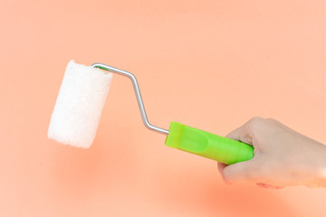 Female hand holding paint roller isolated over orange background