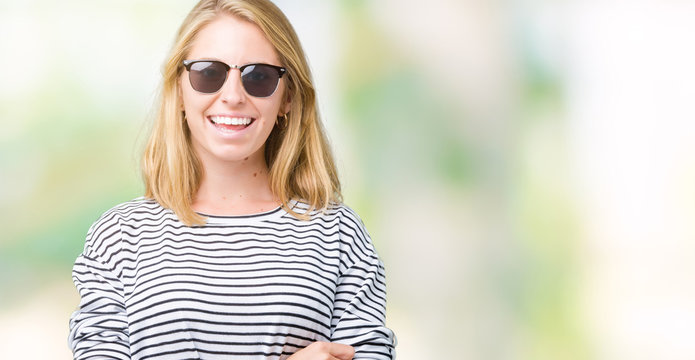 Beautiful young woman wearing sunglasses over isolated background happy face smiling with crossed arms looking at the camera. Positive person.
