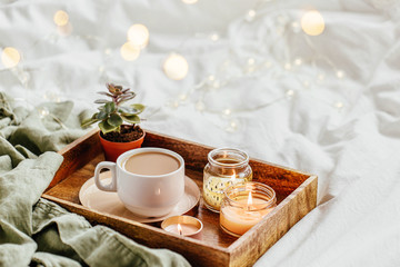 Tray of coffee and candles with warm plaid on white bedding . Breakfast in bed.  Scandinavian style.  Flat lay, top view