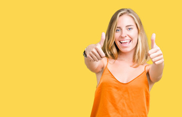 Beautiful young woman wearing orange shirt over isolated background approving doing positive gesture with hand, thumbs up smiling and happy for success. Looking at the camera, winner gesture.