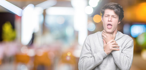 Young handsome sporty man wearing sweatshirt over isolated background shouting and suffocate because painful strangle. Health problem. Asphyxiate and suicide concept.