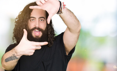 Young man with long hair and beard wearing heavy metal black outfit smiling making frame with hands and fingers with happy face. Creativity and photography concept.